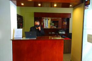 un hombre con una máscara hablando en un teléfono detrás de un mostrador en Crystal Hotel en Salta