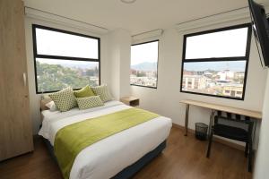 ein Schlafzimmer mit einem Bett, einem Schreibtisch und 3 Fenstern in der Unterkunft Normandía Tower in Bogotá