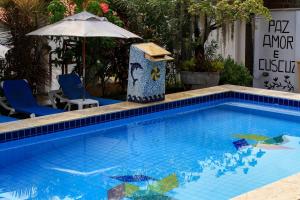 a blue swimming pool with an umbrella and some chairs at Catavento da Pipa in Pipa +44 photos