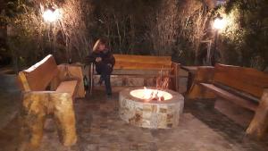 uma mulher sentada num banco ao lado de uma fogueira em Chale de Madeira - Lareira e Fogueira---lindo gramado com mesa para café da manhã, churrasqueira e fogueira em Campos do Jordão