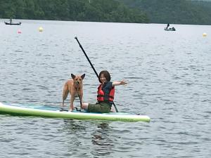 a woman and a dog on a paddle board in the water at Petit Hotel Kazekozou in Shinano