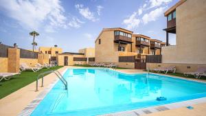 a swimming pool with chairs and a building at Tinajas Chic in Corralejo