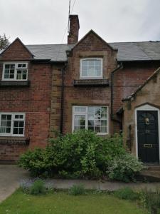 a brick house with a black door and windows at Featherbed Cottage in Coventry