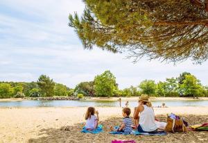 a woman and two children sitting on a beach at Maison océane proche plage in Arès