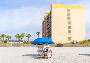 a woman sitting in a chair under an umbrella on the beach at Surfside Beach Oceanfront Hotel in Myrtle Beach