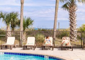 two women sitting in chairs next to a swimming pool at Surfside Beach Oceanfront Hotel in Myrtle Beach
