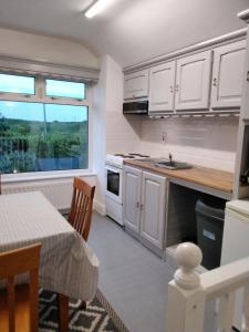 cocina con armarios blancos, mesa y ventana en The Ramblings, en Wexford