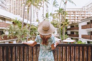 Una ragazza con un cappello in piedi accanto a una recinzione di White Sands Hotel a Honolulu