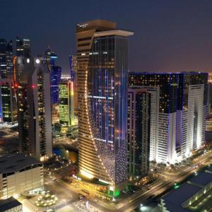 The Bentley Luxury Hotel & Suites في الدوحة: أفق المدينة في الليل مع مبنى طويل