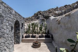 a stone walled patio with a couch and cactus at Nimbus Santorini in Oia