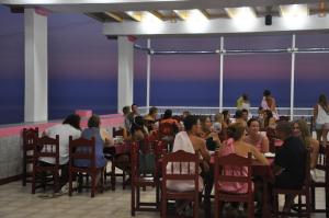 a group of people sitting at tables in a restaurant at Pink Palace Beach Resort in Agios Gordios
