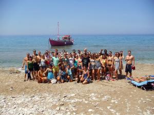 a group of people standing on a beach with a boat at Pink Palace Beach Resort in Agios Gordios