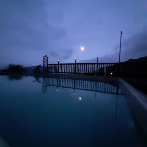 een zwembad van water in de nacht met de maan in de lucht bij wooden Edge Of The Village in Ma'ale Gamla