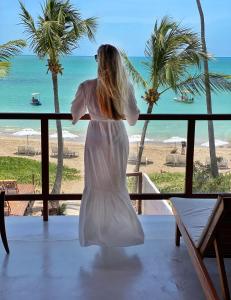 a woman in a white dress looking out at the beach at Pousada Rota Ecológica in Pôrto de Pedras