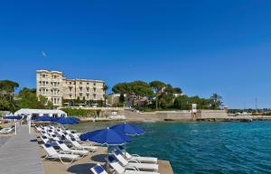a group of lounge chairs and umbrellas next to the water at Hôtel Belles Rives in Juan-les-Pins
