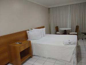 Ponta Negra Flats Partic في ناتال: غرفة نوم بسرير ابيض وطاولة وكراسي