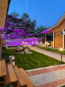 a picnic table in front of a stone wall with purple lights at Eco hotel & restaurant "SKALA" in Borovoye