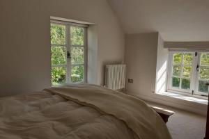 a white bedroom with a bed and two windows at Characterful Cottage adjacent to an Orchard in Brockley