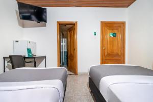 two beds in a room with a desk and a television at Hotel Quintas de Normandia in Bogotá