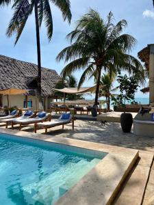 a swimming pool with lounge chairs and palm trees at Paje Beach Apartments & Hotel in Paje