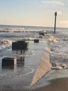 a beach with waves and a lighthouse in the ocean at The Hideout in Anderby
