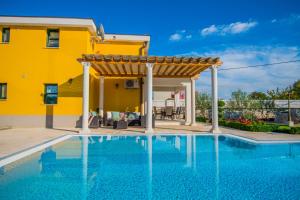a pool with a pergola and a yellow house at Holiday Home Petra in Donji Proložac
