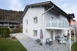 Cette maison blanche dispose d'une terrasse avec une table et des chaises. dans l'établissement Schönes Ferienhaus mit Garten, à Pörtschach am Wörthersee