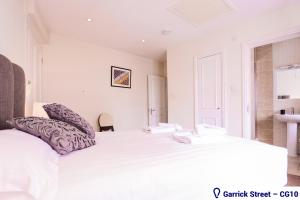 a white bedroom with a large white bed with purple pillows at Stayo Covent Garden in London