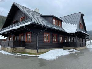 a black house with snow on the roof at Apartmány NETA Velké Karlovice, Polanský Dvůr in Velké Karlovice