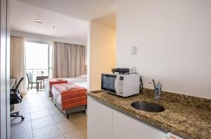 uma cozinha com um lavatório e um quarto com uma cama em Flat 1506 - Studio duplo a 600m da Petrobras em Imbetiba em Macaé