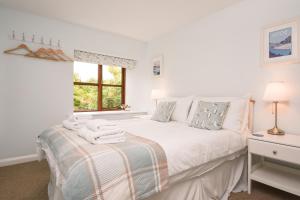 a white bedroom with a bed and a window at Lily Cottage in Looe