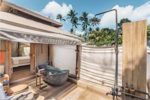 a bathroom with a tub and a bedroom with palm trees at Khwan Beach Resort - Luxury Glamping and Pool Villas Samui - Adults Only - SHA Extra Plus in Mae Nam