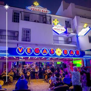 een menigte mensen die 's nachts buiten een versace bar zitten bij Vegas Residence in Albufeira