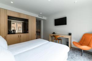 a bedroom with a white bed and an orange chair at Hotel Le Bois De Bruges in Bruges