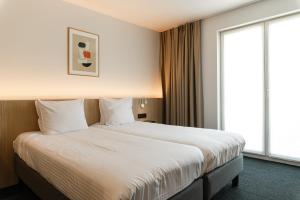 a large bed in a hotel room with a large window at Hotel Le Bois De Bruges in Bruges