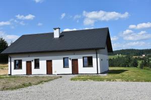 a small white house with a black roof at Zagroda Wataha 782 305 923 in Polańczyk