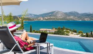 a woman sitting in a chair with a laptop next to a pool at Ionian Grand Villas - Villa Estella in Lygia