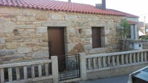 een stenen gebouw met een hek en een deur bij O Iniño casita rural costera in O Grove