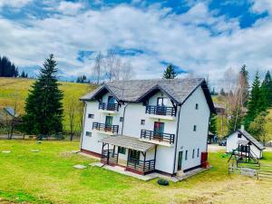 a white house with a black roof on a green field at Pensiunea Cassandra in Neagra Şarului