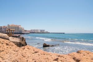 una playa con rocas y el océano y edificios en Alquilaencanarias-El Medano Delfines-2 rooms en El Médano