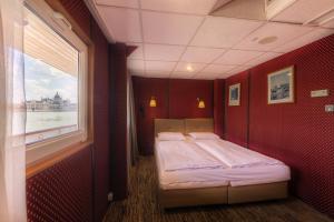 ein Schlafzimmer mit einem Bett in einem roten Zimmer mit einem Fenster in der Unterkunft Grand Jules - Boat Hotel in Budapest