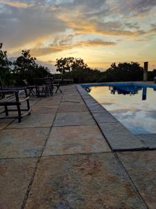 a swimming pool with benches and a sunset in the background at Palma Adventure Hostel in Barreirinhas
