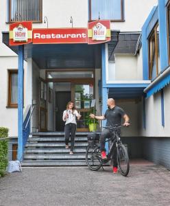 Ein Mann und eine Frau auf einem Fahrrad vor einem Gebäude in der Unterkunft Hotel Scirocco in Baunatal