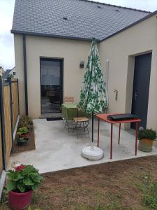 un patio con una mesa y una sombrilla junto a una casa en Proche GR34 , Studio "Estrella" , petit cocon accueillant en Hillion