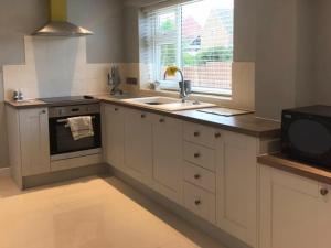 a kitchen with white cabinets and a sink and a window at Pet-Friendly - 2 Bedrooms Bungalow hot tub parking in Heacham