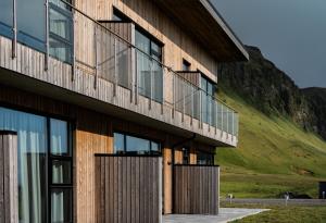 a building with a green hill in the background at Black Beach Suites in Vík