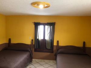 2 Betten in einem Zimmer mit gelben Wänden und einem Fenster in der Unterkunft San Pablo in Pátzcuaro