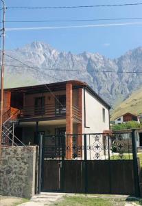 ein Haus mit einem Zaun und Bergen im Hintergrund in der Unterkunft Wander Kazbegi Hotel in Kazbegi