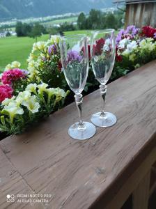 two wine glasses sitting on a wooden table with flowers at Haus Mühlenheim in Schwendau