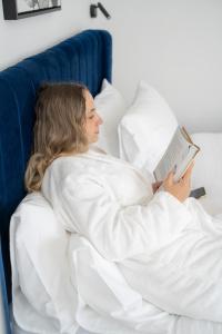 De' Mar Florentine Hotel By Peraia في تل أبيب: امرأة مستلقية على السرير تقرأ كتابا